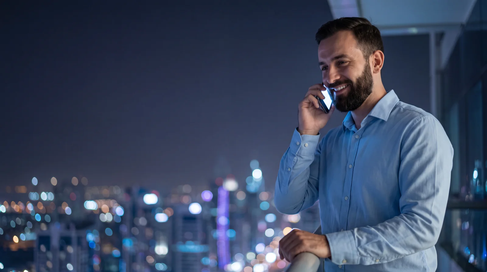 A Pakistani man on a balcony in Dubai at night, calling home