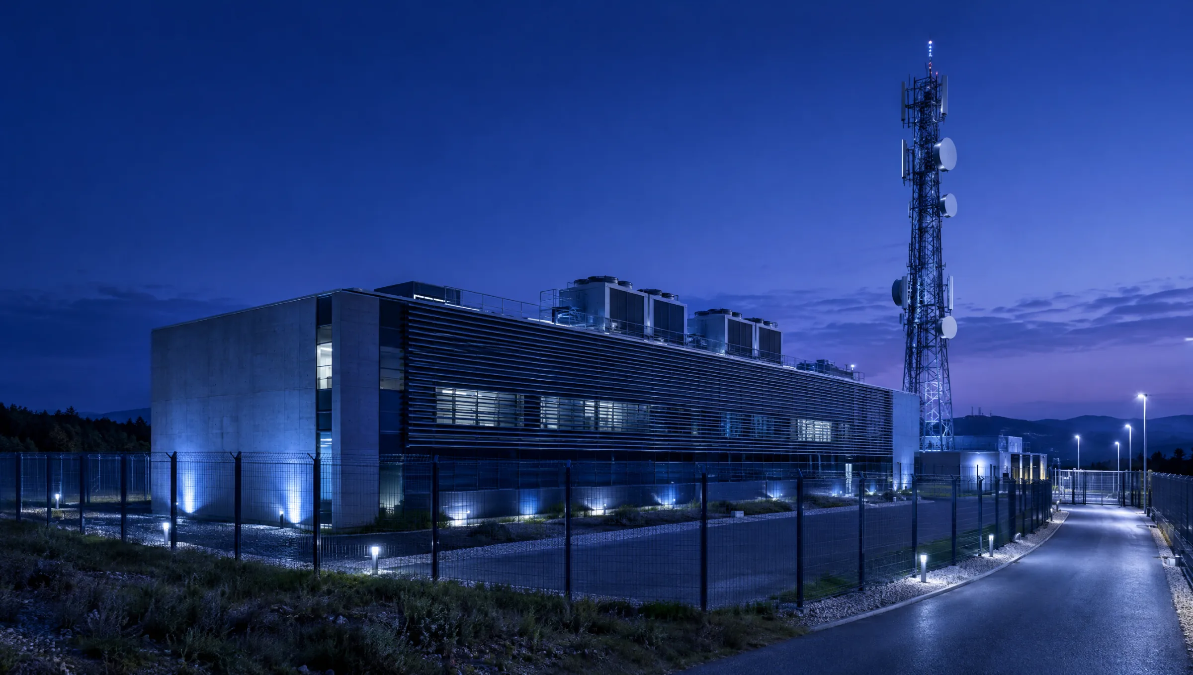 A telecom gateway building at dusk beside a communications tower with microwave dishes